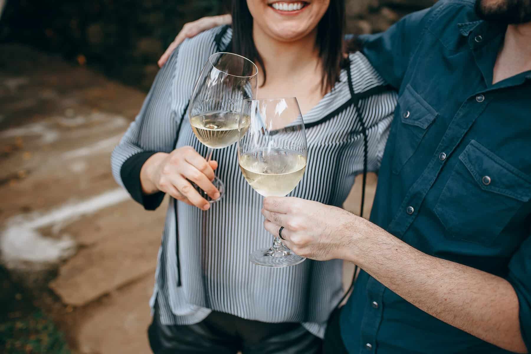 Two friends toasting with glasses of white wine in an outdoor setting, celebrating a joyful occasion.