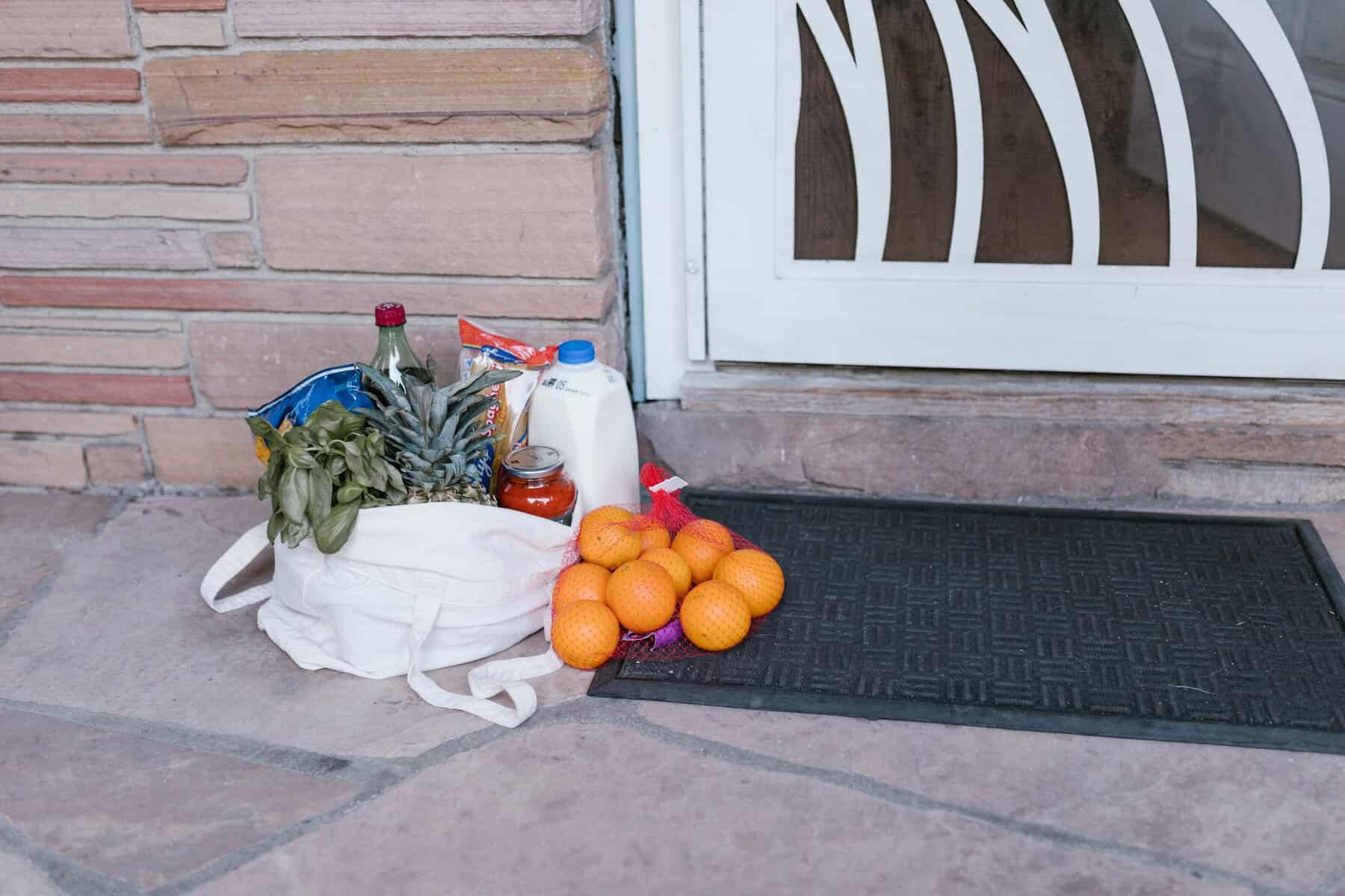 Reusable bag with groceries and fruits left at doorstep, highlighting delivery service.