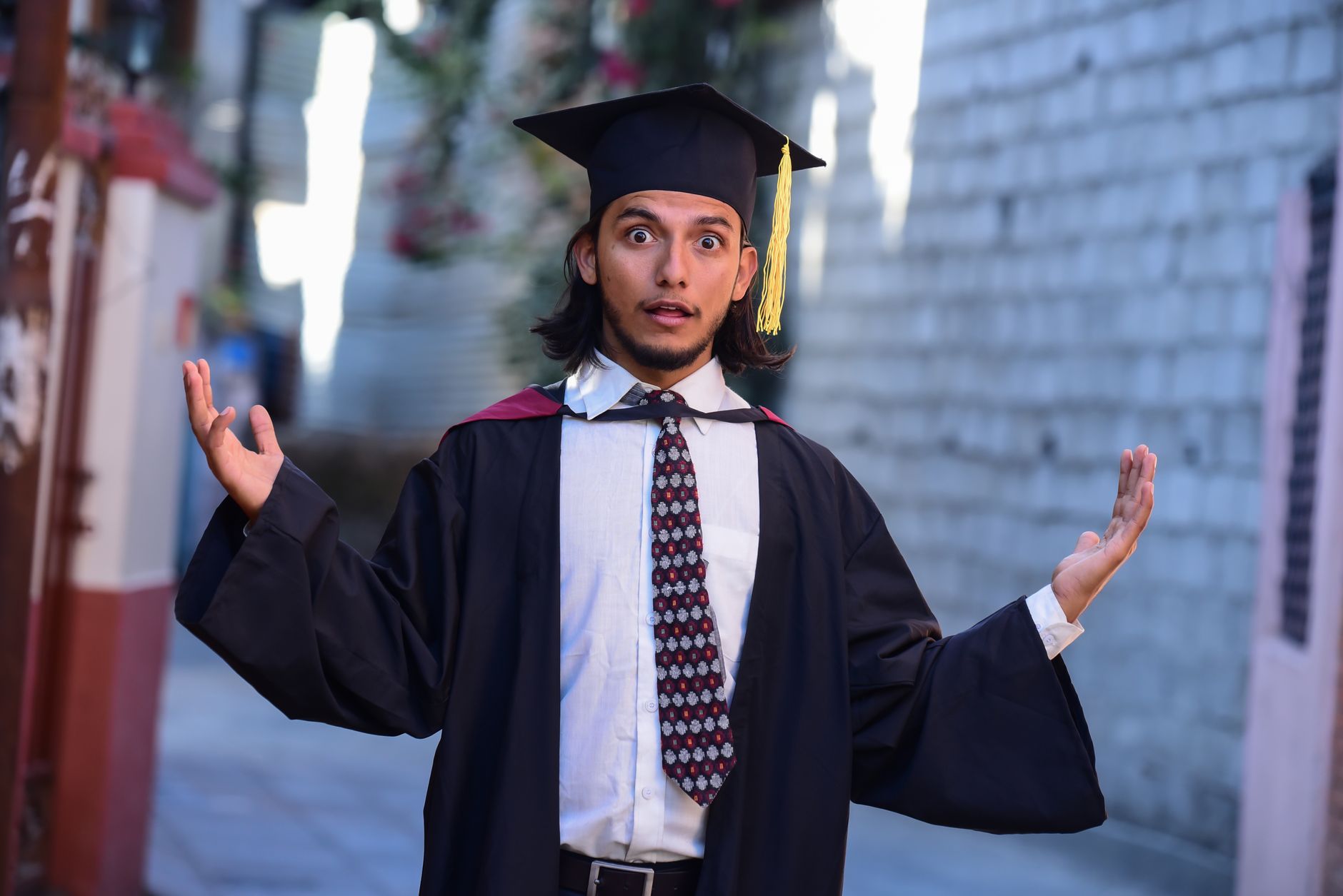A surprised graduate poses outdoors in cap and gown, celebrating academic achievement.